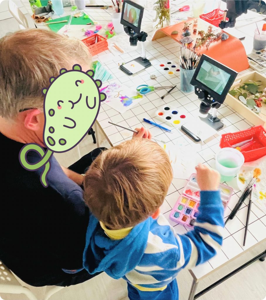Parent et enfant observent des éléments végétaux avec un microscope lors d’un atelier artistique à l’Artorium